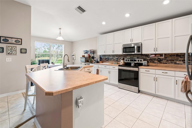 kitchen featuring white cabinets, stainless steel appliances, tasteful backsplash, an island with sink, and sink