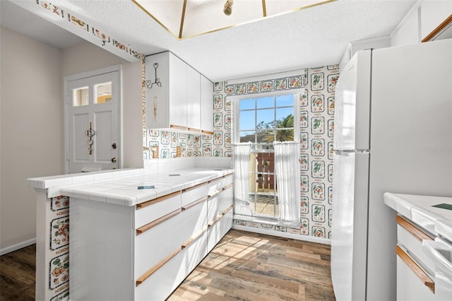 kitchen with hardwood / wood-style floors, white cabinets, white refrigerator, a textured ceiling, and tile counters