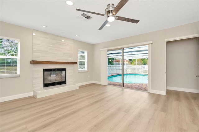 unfurnished living room featuring a wealth of natural light, a tile fireplace, ceiling fan, and light hardwood / wood-style flooring