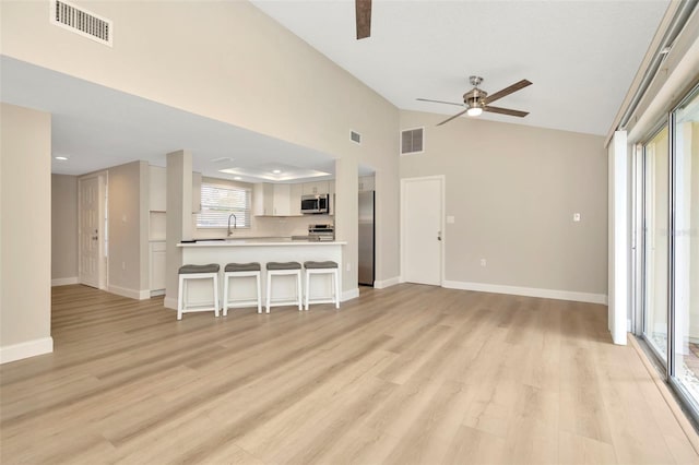 unfurnished living room featuring high vaulted ceiling, ceiling fan, sink, and light hardwood / wood-style floors