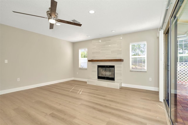 unfurnished living room featuring a wealth of natural light, a textured ceiling, a tile fireplace, and light hardwood / wood-style flooring