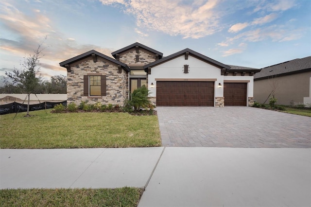 view of front of property featuring decorative driveway, a yard, stucco siding, an attached garage, and stone siding