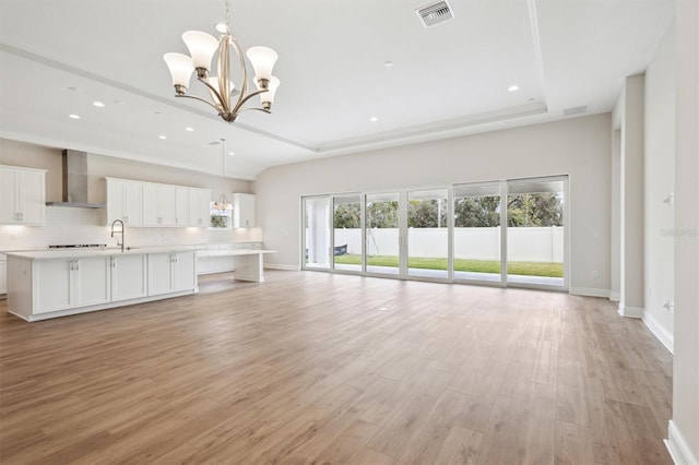 unfurnished living room with baseboards, visible vents, a raised ceiling, light wood-style floors, and a notable chandelier