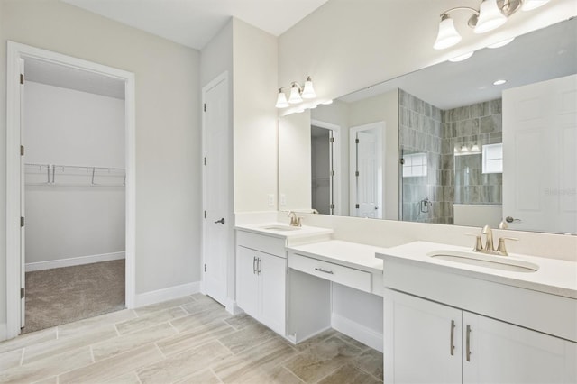 bathroom with a walk in closet, tiled shower, a sink, and double vanity