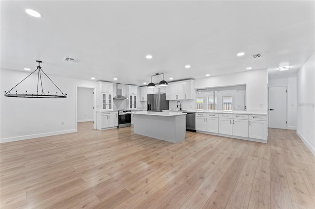 kitchen with stainless steel appliances, light hardwood / wood-style flooring, white cabinets, wall chimney range hood, and pendant lighting