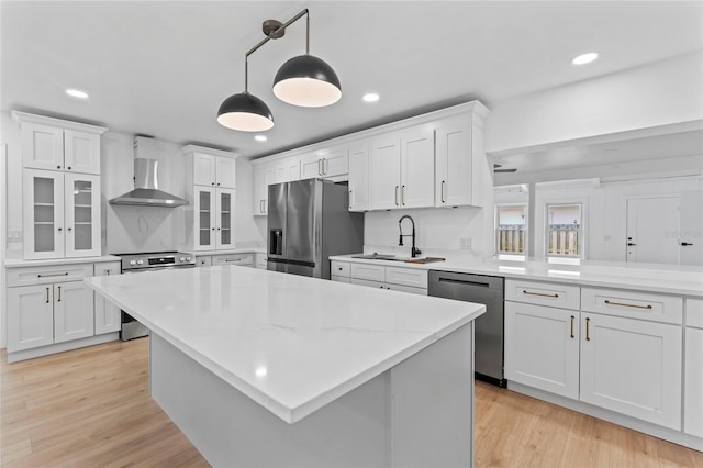 kitchen featuring wall chimney range hood, white cabinetry, decorative light fixtures, and appliances with stainless steel finishes