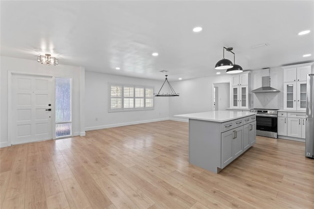 kitchen with stainless steel appliances, light hardwood / wood-style floors, a center island, wall chimney exhaust hood, and hanging light fixtures