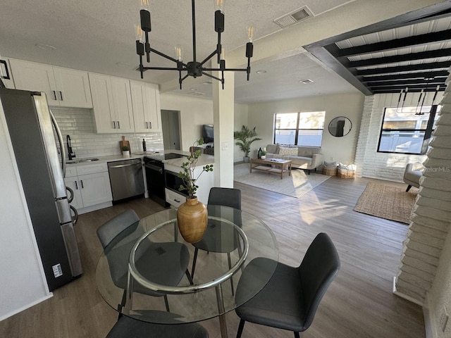 dining space with hardwood / wood-style floors, brick wall, a textured ceiling, and a chandelier