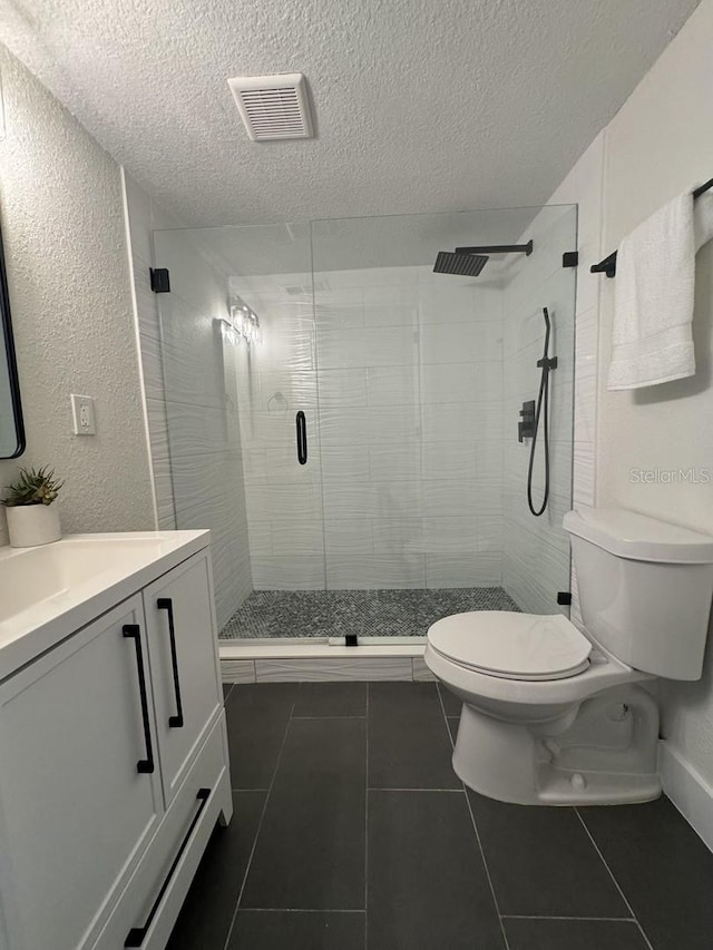 bathroom featuring toilet, a shower with door, tile patterned flooring, a textured ceiling, and vanity