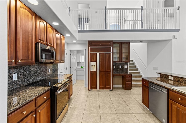 kitchen with dark stone counters, appliances with stainless steel finishes, light tile patterned floors, and washer / dryer