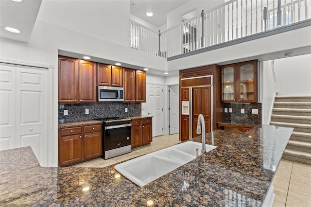 kitchen with stainless steel appliances, sink, tasteful backsplash, dark stone countertops, and a towering ceiling