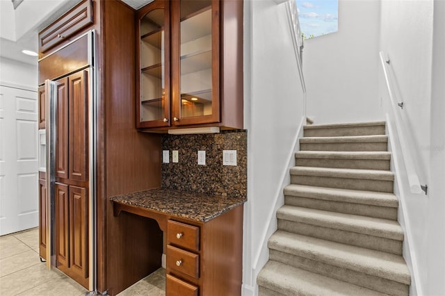 interior space with dark stone counters, decorative backsplash, built in desk, and light tile patterned flooring