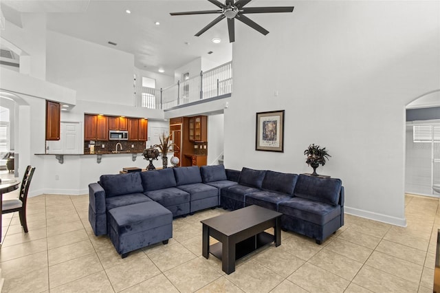 living room featuring light tile patterned flooring, ceiling fan, a high ceiling, and a healthy amount of sunlight