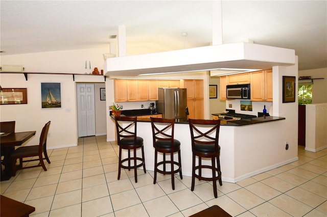 kitchen with kitchen peninsula, lofted ceiling, a kitchen bar, and appliances with stainless steel finishes