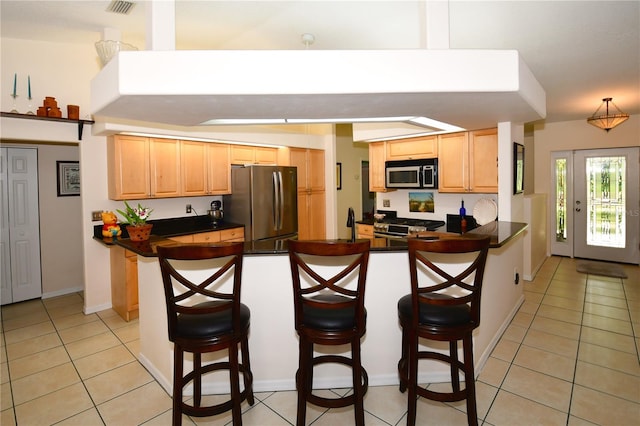 kitchen featuring stainless steel appliances, a breakfast bar, kitchen peninsula, light brown cabinets, and light tile patterned floors