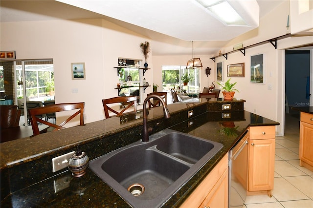 kitchen with dishwasher, dark stone counters, light tile patterned floors, and a healthy amount of sunlight