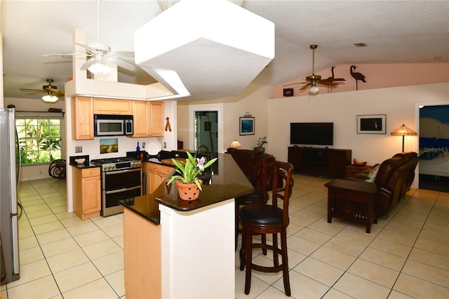 kitchen with lofted ceiling, kitchen peninsula, light tile patterned floors, a kitchen breakfast bar, and appliances with stainless steel finishes