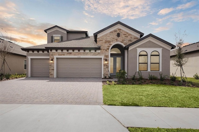 view of front of home featuring an attached garage, a yard, stone siding, decorative driveway, and stucco siding