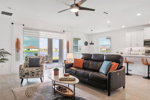 living room featuring ceiling fan, light hardwood / wood-style floors, ornamental molding, and sink