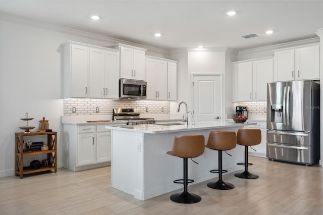 kitchen featuring backsplash, white cabinetry, stainless steel appliances, and a kitchen island with sink