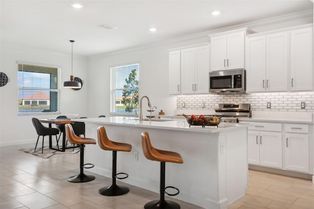 kitchen with appliances with stainless steel finishes, a kitchen island with sink, sink, white cabinetry, and hanging light fixtures