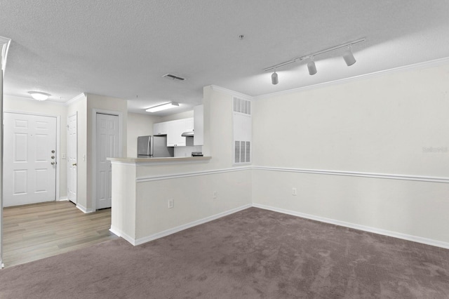 interior space featuring a textured ceiling, rail lighting, crown molding, and carpet floors