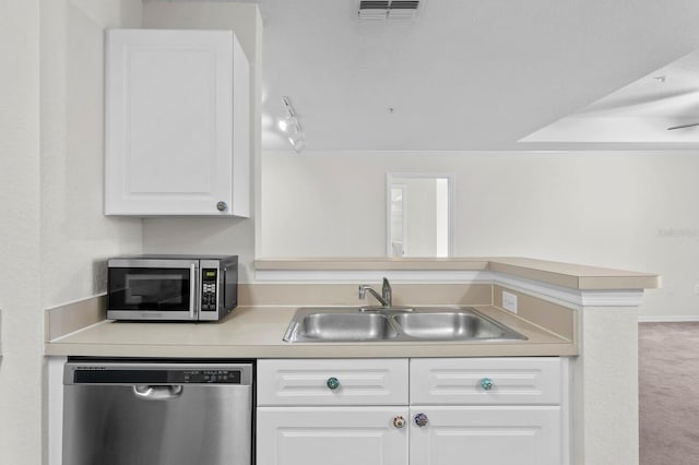 kitchen with stainless steel appliances, kitchen peninsula, carpet floors, sink, and white cabinetry