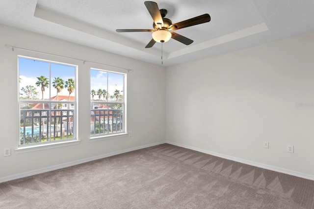 carpeted empty room with ceiling fan, a textured ceiling, and a raised ceiling