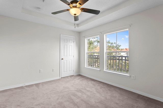 empty room featuring ceiling fan, light carpet, and a tray ceiling