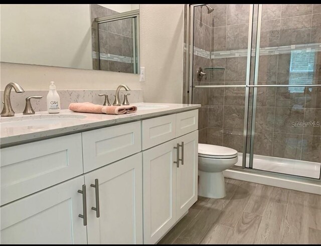 bathroom with wood-type flooring, vanity, toilet, and a shower with door