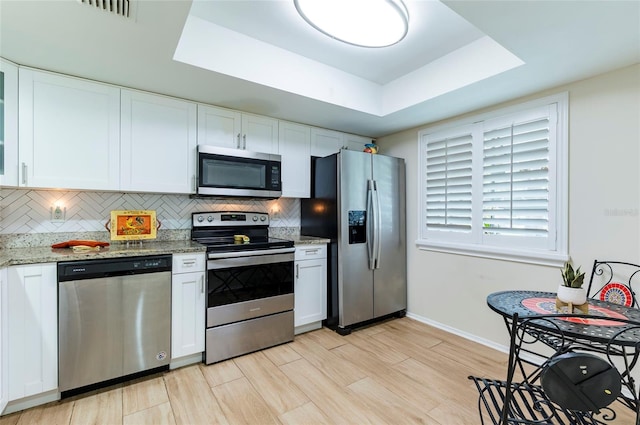 kitchen featuring light stone counters, stainless steel appliances, white cabinetry, light hardwood / wood-style floors, and a tray ceiling