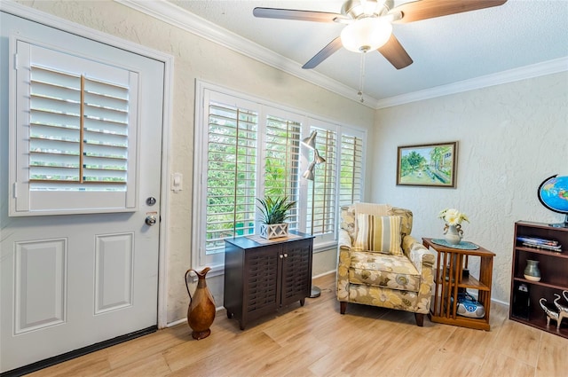 living area with a textured ceiling, light wood-type flooring, ceiling fan, and crown molding