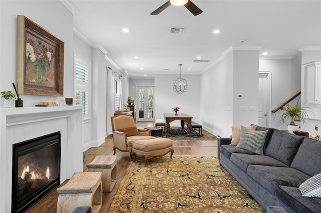 living room featuring hardwood / wood-style floors, a tiled fireplace, ceiling fan with notable chandelier, and ornamental molding