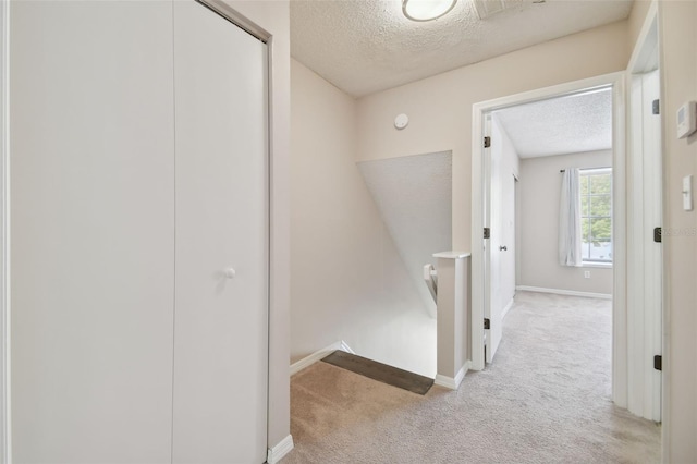 hall featuring light colored carpet and a textured ceiling