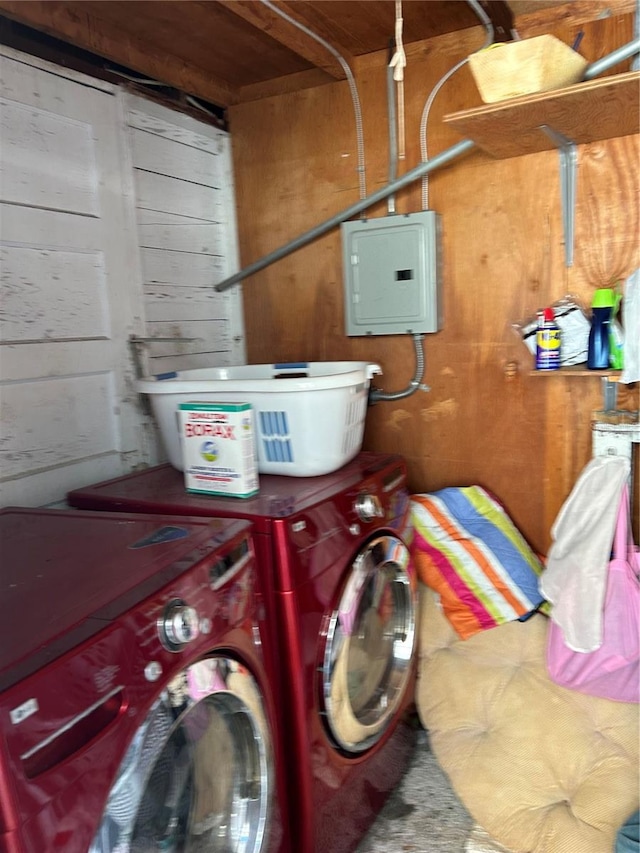 clothes washing area with wood walls, electric panel, and washer and dryer