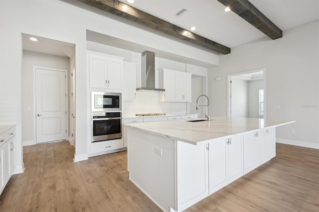 kitchen featuring oven, a sink, white cabinetry, wall chimney range hood, and a large island with sink