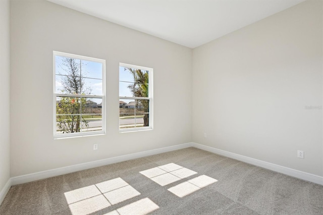 empty room featuring light carpet, plenty of natural light, and baseboards