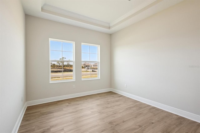 empty room featuring light wood-type flooring, baseboards, a raised ceiling, and ornamental molding