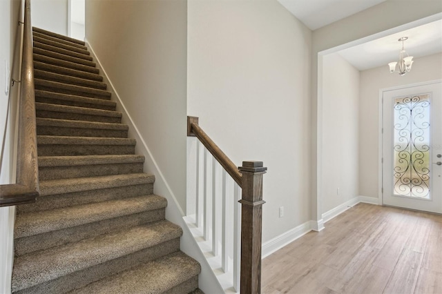 stairway with a notable chandelier, wood finished floors, and baseboards