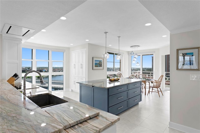 kitchen featuring a center island with sink, a water view, light stone counters, ornamental molding, and hanging light fixtures