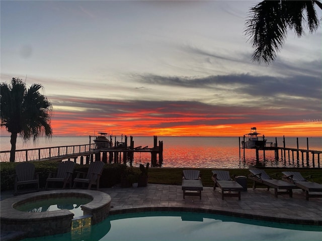 pool at dusk with a patio area, an in ground hot tub, and a water view