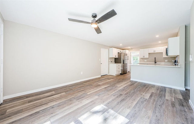 unfurnished living room featuring light hardwood / wood-style floors, ceiling fan, and sink