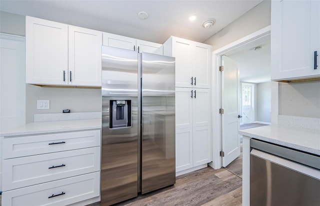 kitchen with light stone countertops, stainless steel fridge, white cabinetry, and light wood-type flooring