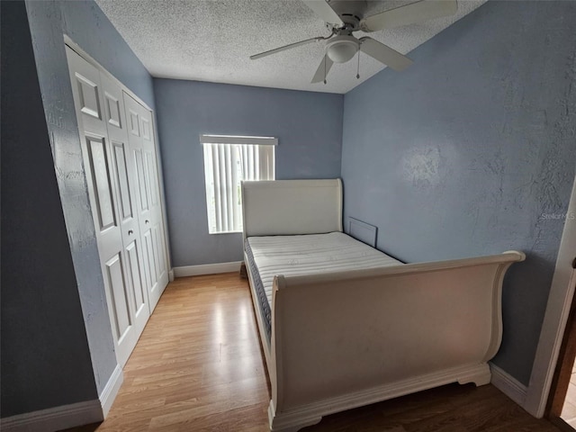 unfurnished bedroom with ceiling fan, a textured ceiling, a closet, and light wood-type flooring