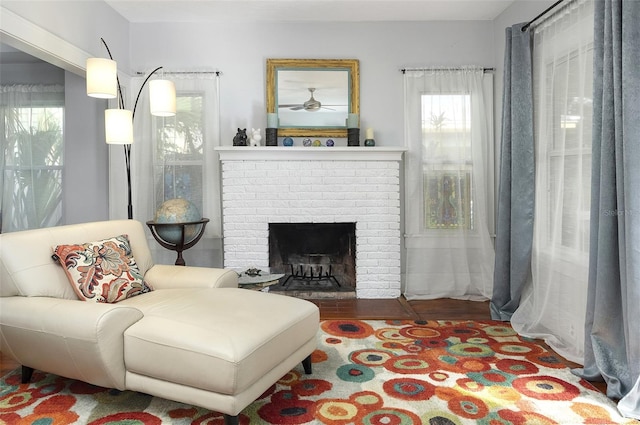 sitting room featuring a brick fireplace, a wealth of natural light, ceiling fan, and hardwood / wood-style flooring