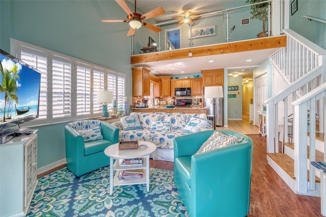 living room with light hardwood / wood-style floors, ceiling fan, and a high ceiling