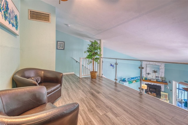 living area with a stone fireplace, wood-type flooring, and vaulted ceiling