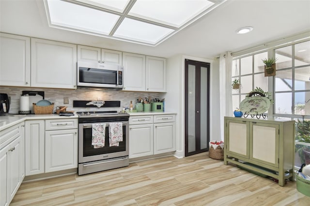 kitchen with tasteful backsplash, white cabinets, light wood-type flooring, and appliances with stainless steel finishes