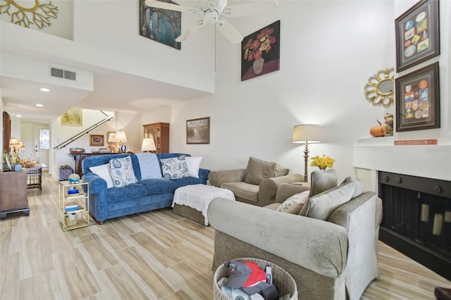 living room featuring a towering ceiling, light wood-type flooring, and ceiling fan