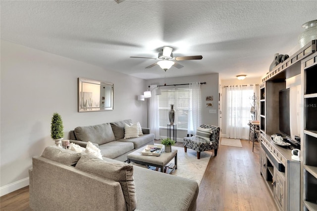 living room with ceiling fan, a textured ceiling, and light wood-type flooring